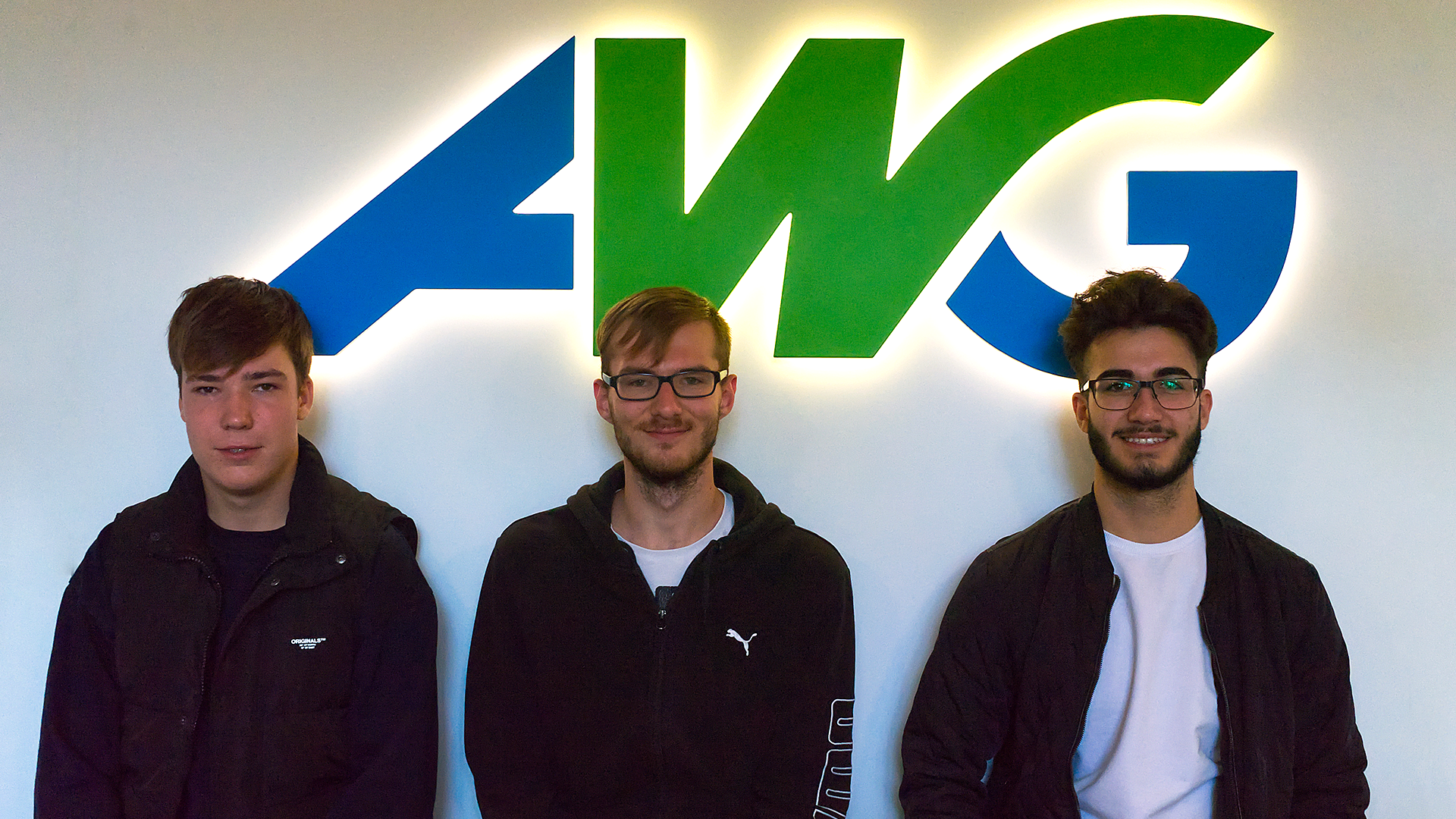 Die drei neuen Auszubildenden vor dem AWG Logo