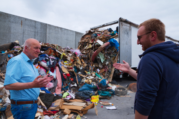 Ein LKW entlädt seine Fracht - 36 Tonnen Abfälle. Im Vordergrund beraten sich zwei Mitarbeiter der AWG über das weitere Vorgehen.
